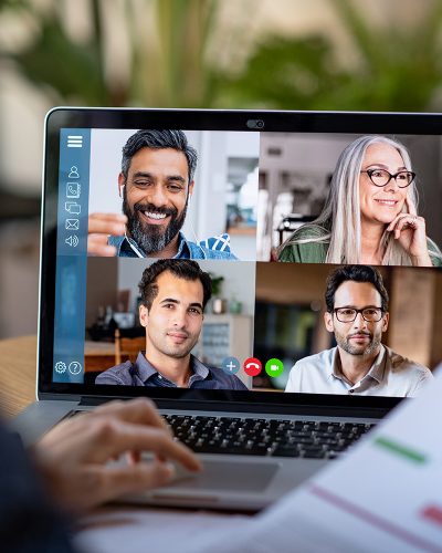 Back view of business woman talking to her colleagues about business plan in video conference. Multiethnic business team using laptop for a online meeting in video call. Group of buinessmen and businesswomen smart working from home.